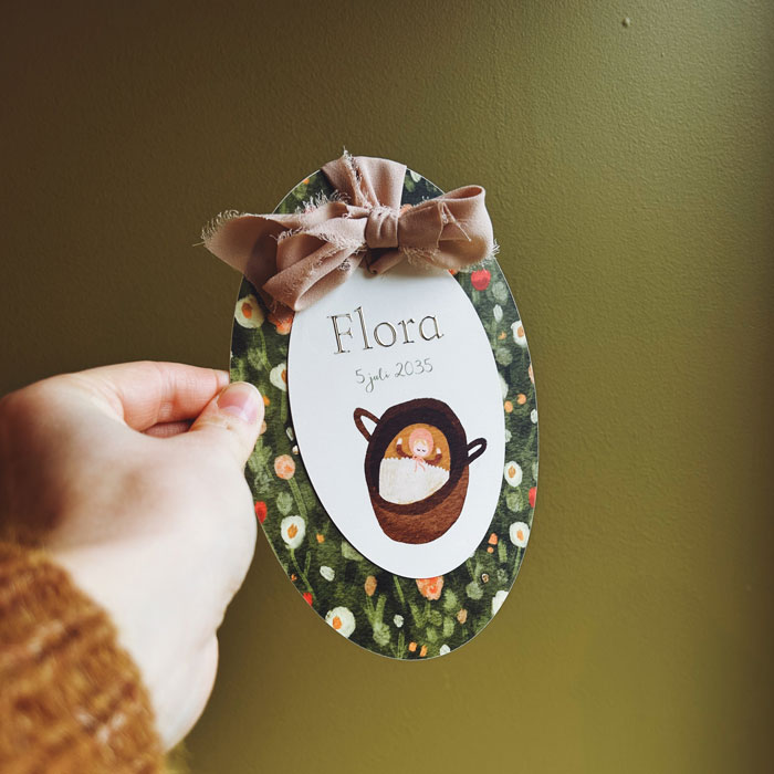 Geboortekaartje met label, bloemenveld en wiegje