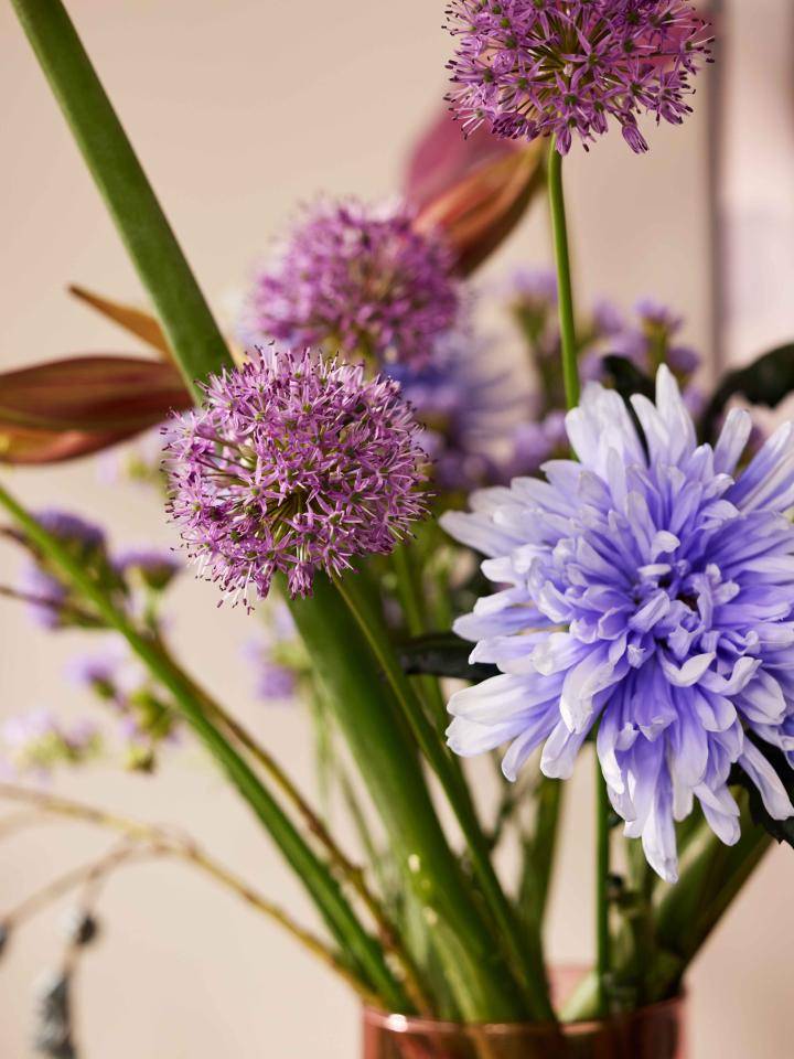 Close-up van een boeket met paarse alliums en een grote blauwe chrysant, met groene stelen en bladeren.