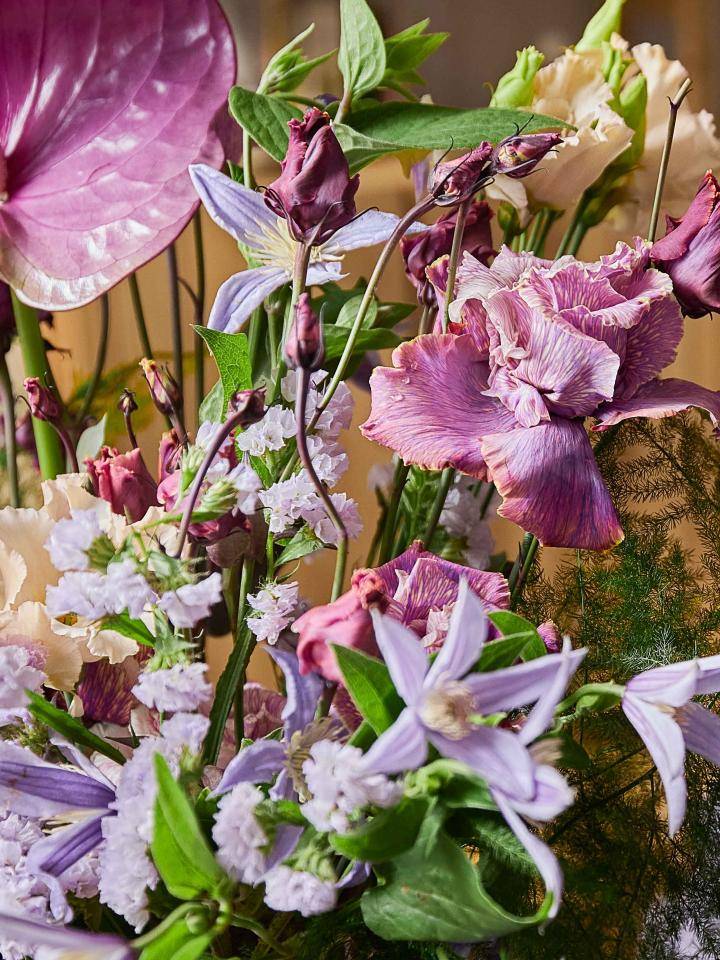Diverse boeket met roze anthuriums, paarse irissen, lichtpaarse clematis en kleine witte bloemen, omringd door groen blad.