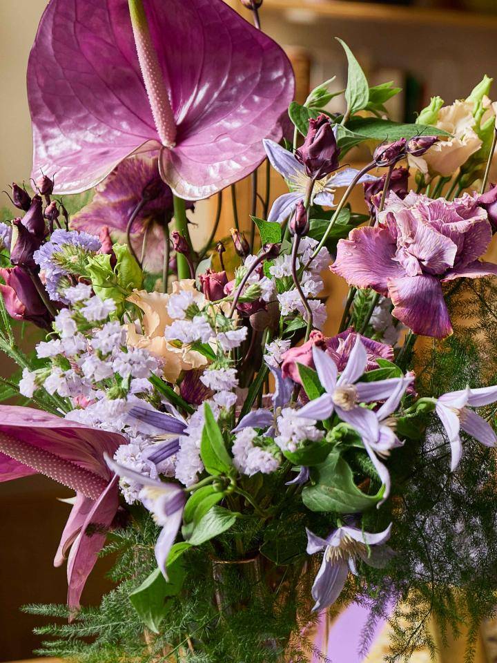 Boeket met grote paarse anthuriums, omringd door kleinere roze, paarse en witte bloemen, met groen blad, binnenshuis.