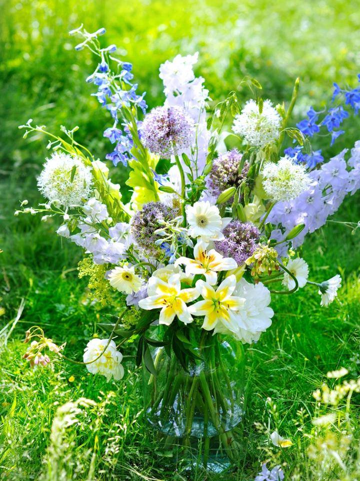 Hand schikt kleurrijk midzomerboeket met diverse bloemen op een houten tafel.