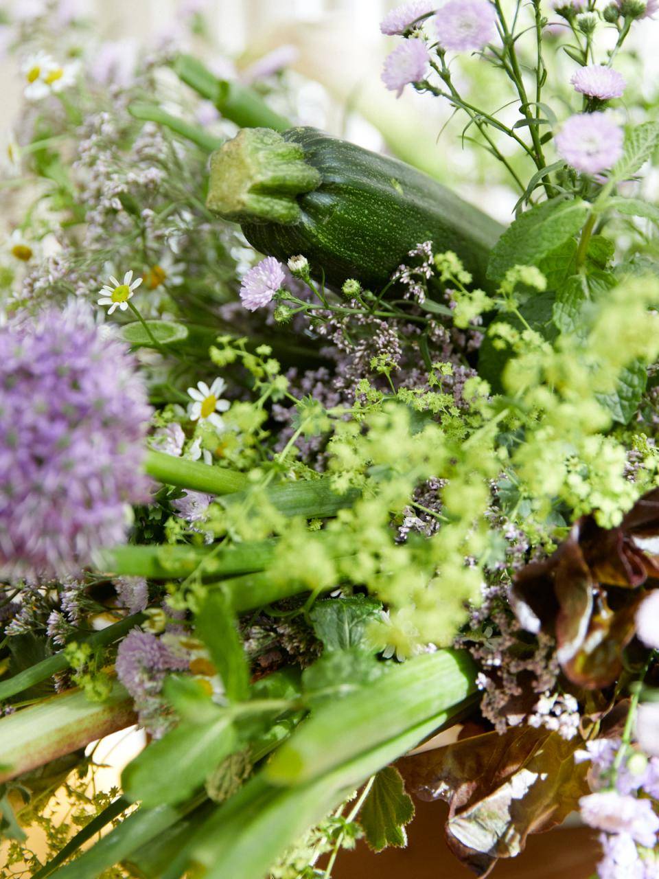 Boeket van paarse en witte bloemen, groene bladeren en een courgette.
