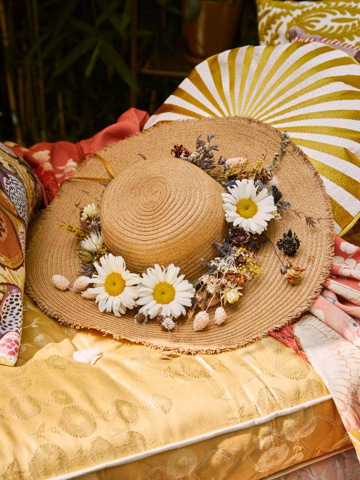 Strohoed versierd met witte madeliefjes en gedroogde bloemen op geel-gouden stof.