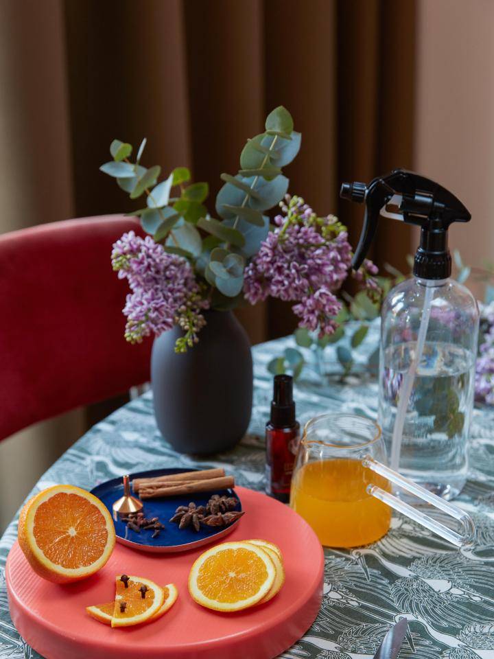 DIY winter homespray ingrediënten: gesneden sinaasappels, kaneelstokjes, kruidnagels en eucalyptus in een vaas.
