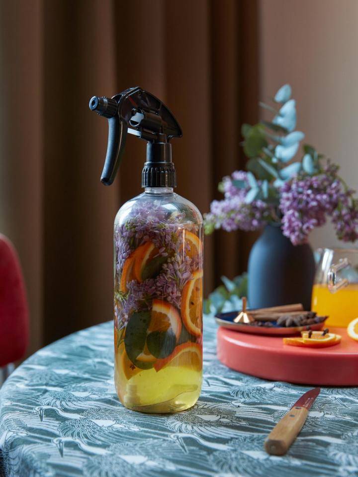 DIY warme winter homespray in glazen fles met kruiden en bloemen op houten tafel.