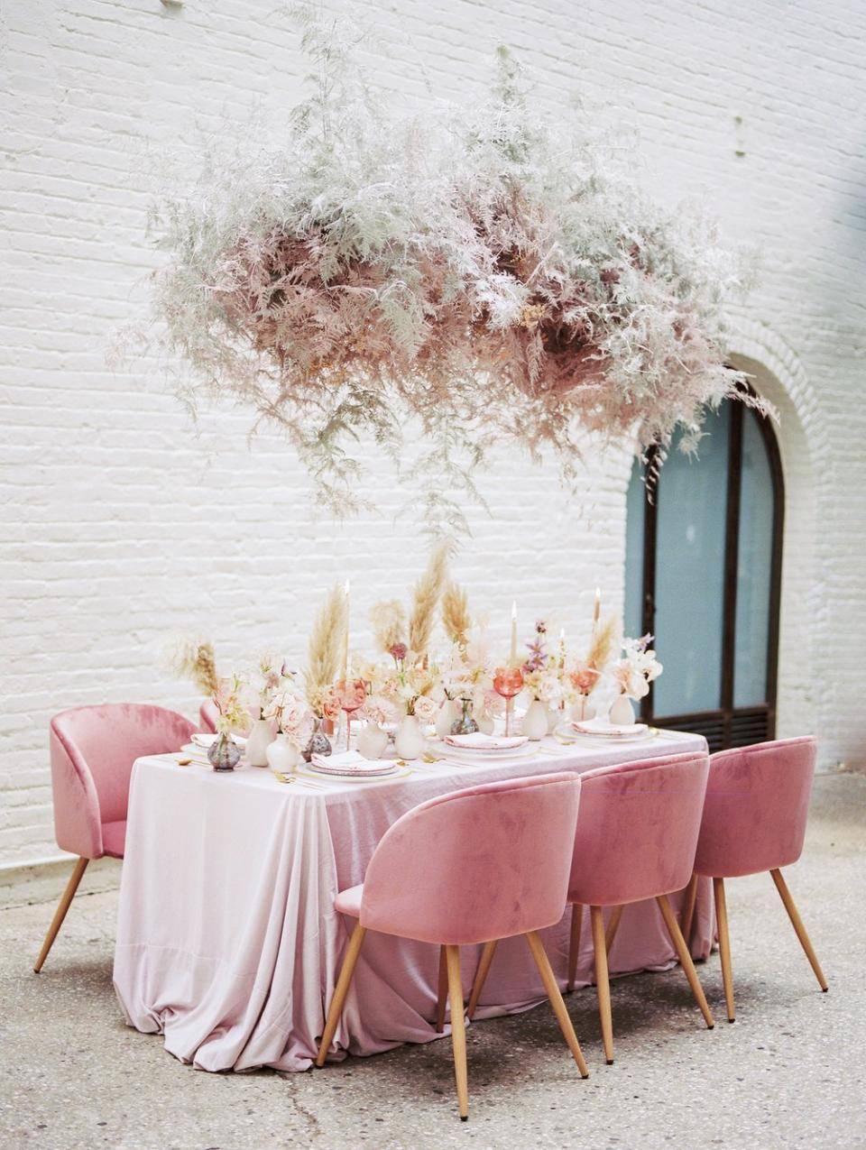 Eettafel met roze tafelkleed en bloemenarrangementen, omringd door roze fluwelen stoelen.