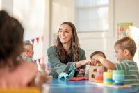 Vrouw speelt en bouwt samen met jonge kinderen aan tafel met kleurrijk speelgoed.