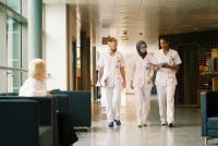 Drie zorgprofessionals lopen overleggend door een ziekenhuisgang met dossiers en tablet.